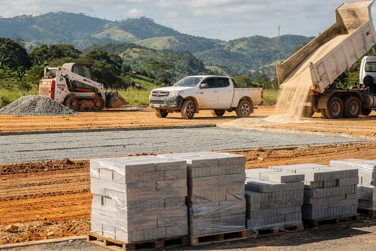 Caminhonete, minicarregadeira e caminhão caçamba em obra de pavimentação
